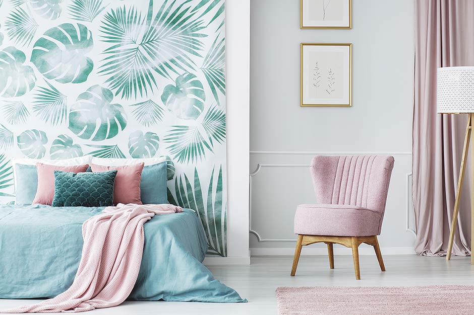 Bedroom with leafy accent wall and pink chair.